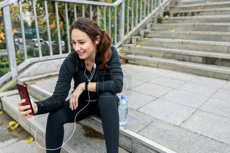 Téléchargez les photos : Jeune femme qui fait une pause après avoir fait de l'exercice et écouté de la musique sur un escalier. Concept de personnes actives occasionnelles - en image libre de droit