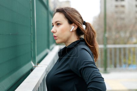 Téléchargez les photos : Jeune sportive portant des écouteurs et se tenant dehors dans la ville après sa course matinale - en image libre de droit