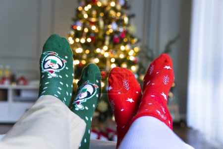 Photo for Woman and man legs in Christmas socks front of glitter Christmas tree - Royalty Free Image