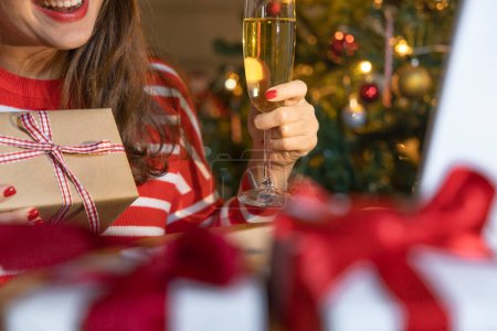 Téléchargez les photos : Joyeux jeune femme toasting avec Champagne tout en faisant appel vidéo sur ordinateur portable le soir de Noël à hom - en image libre de droit