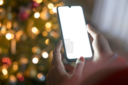Foto de Cortado de las manos de la mujer sosteniendo el teléfono inteligente en Navidad. Teléfono móvil digital con área de espacio de copia - Imagen libre de derechos