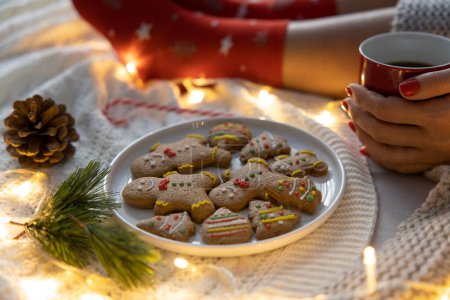 Photo for Young woman drinking a cup of coffee with her cute gingerbread cookies in her bed. Christmas, relaxation concept - Royalty Free Image