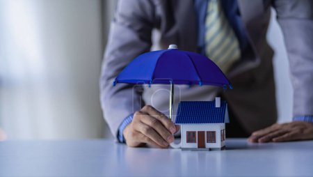 a businessman spreading a blue umbrella for the house Real estate, insurance and property concepts