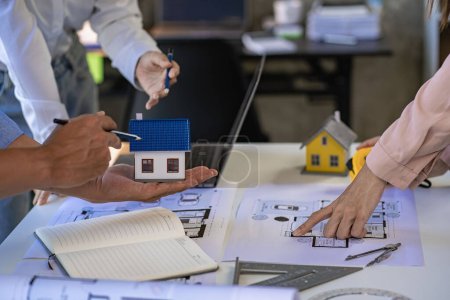 Architekten und Ingenieure zeigen auf Baupläne und zeichnen mit Laptops Hausentwürfe in einem Konstruktionsbüro.