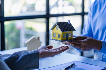 Téléchargez les photos : Le concept d'achat d'une maison, l'agent propose des contrats de taux d'intérêt sur les hypothèques et les achats de maisons pour les clients de signer des contrats avec des agents immobiliers. - en image libre de droit