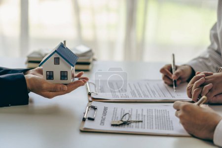 Photo for House purchase concept, real estate agent with house model talking to client about buying home insurance and client signing contract under formal contract agreement with real estate law - Royalty Free Image