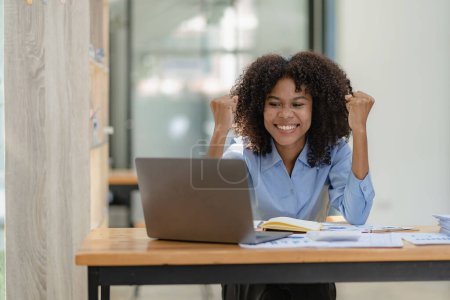 African American businesswoman in suit reads good news about young smart accountant sitting in colleague while looking at laptop She raised her fist, cheering for the success of her project. Poster 650581532