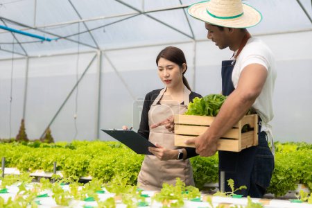 Two Asian man and woman working in hydroponic vegetable farm walking, inspecting and harvesting happily. Male and female farmer holding green salad box looking at camera with smile in greenhouse farm Stickers 655218228