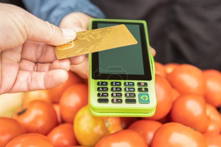 Téléchargez les photos : Le client paie dans une épicerie locale de fruits et légumes avec la technologie nfc de carte de crédit - technologie NFC sans contact. Monnaie et concept financier - Objectif sélectif - en image libre de droit
