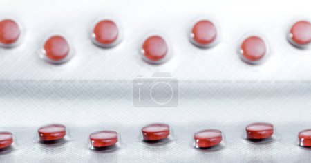 Foto de Pastillas de color rojo dispuestas en un crudo. Línea de enfoque en primer plano. Fabricación de envases farmacéuticos. - Imagen libre de derechos