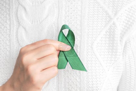 Insignia verde en las manos de las mujeres para apoyar la causa del cáncer. Concepto asistencia sanitaria