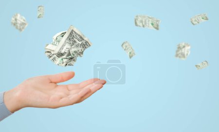 Crumpled one dollar bills flying over female hand on blue background