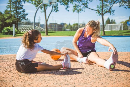 A Mother and little daughter tretching outside in basketball playground