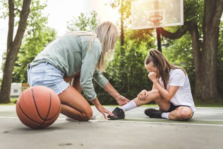 Una madre y su hijita juegan baloncesto afuera llorando por un accidente en el tobillo
