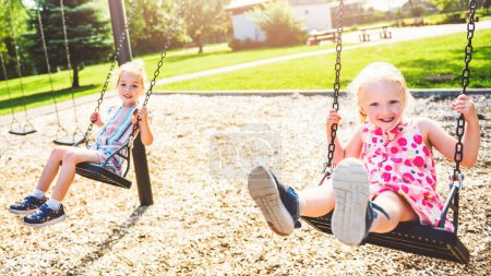zwei glückliche 3-jährige Mädchen auf einer Schaukel. Glückliche Kinder auf dem Spielplatz