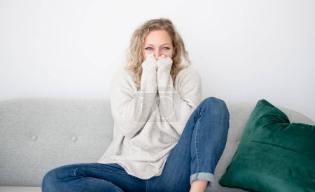 A woman freezing sitting on sofa having symptoms coughing at home, flu concept