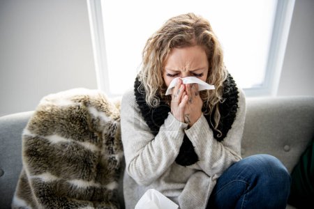 krank verärgerte junge Frau sitzt auf Sofa mit Decke bedeckt frierend weht laufende Nase bekam Fieber erkältet Niesen in Gewebe, krankes Mädchen mit Grippe-Symptomen zu Hause husten, Grippe-Konzept