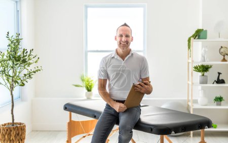 A smiling chiropractor holding pad in hospital and looking at camera