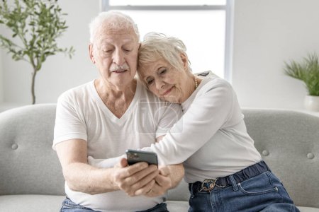 A senior retired couple having great moment together on cozy sofa using cellphone