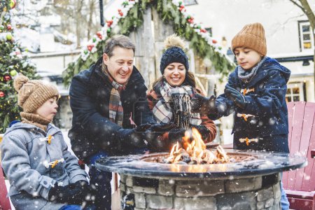 A family with two little son having fun together outdoor on frosty day close to a fire