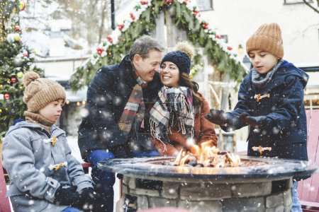 Una familia con dos hijitos divirtiéndose juntos al aire libre en un día helado cerca de un fuego