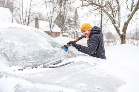 Un jeune homme nettoie sa voiture après une chute de neige par une journée ensoleillée et glacée