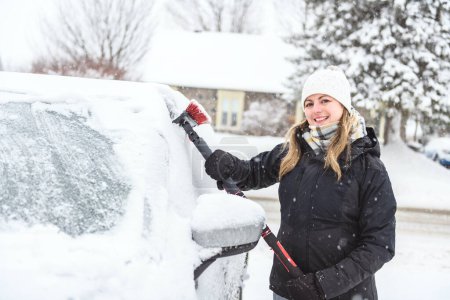 Una mujer limpia su coche después de una nevada en un día soleado y helado