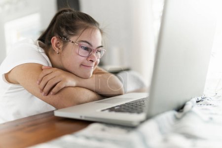 Una niña que tiene un gran tiempo sentarse en la mesa de la cocina con el ordenador portátil