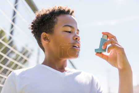 Un niño está usando un inhalador de asma en el parque
