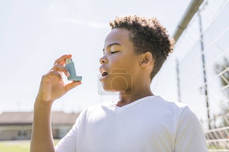 Un niño está usando un inhalador de asma en el parque