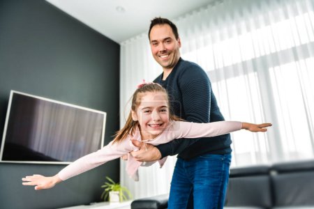 A Dad with his cute little girl on a modern house having fun doing air plane on the living room