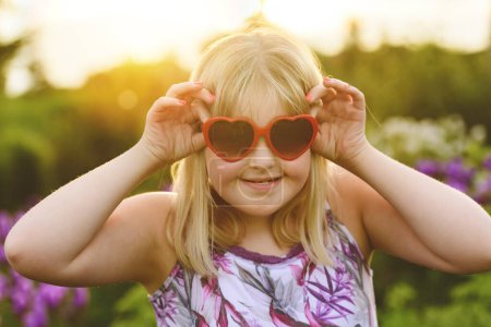 A portrait of child girl outside in summer season at the sunset with love sunglasses