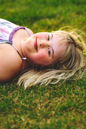 A portrait of child girl outside in summer season at the sunset lay on the grass