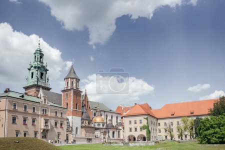 Zabytkowy Zamek na Wawelu w słoneczny dzień w Krakowie, kultowy Zamek na Wawelu w Krakowie, położony na szczycie bujnego zielonego wzgórza pod błękitnym niebem.