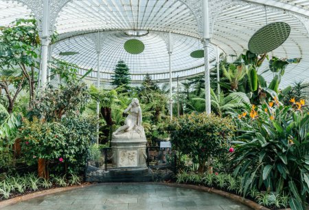 A serene view inside the Glasgow Botanical Gardens Victorian glasshouse, featuring a classic statue surrounded by an array of exotic plants