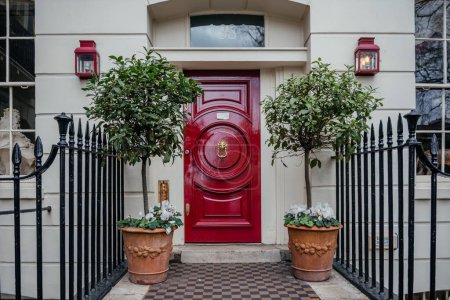 a classic and inviting entrance to a home featuring a bold red door, accented by symmetrical potted plants with topiaries and blooming white flowers