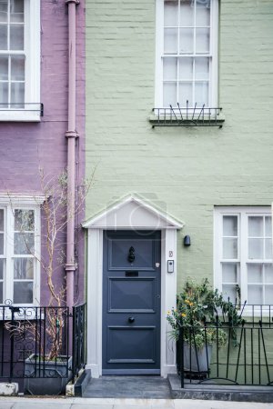 The image showcases the urban charm of London townhouses, with a focus on the contrasting pastel lavender and sage green exteriors complemented by a sophisticated charcoal grey front door