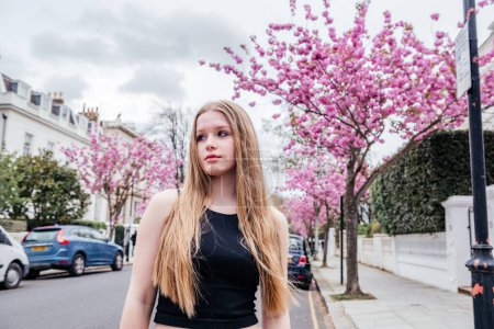 eine junge Frau, die eine Londoner Straße entlang geht, eingerahmt von den atemberaubenden rosa Kirschblüten im Hintergrund