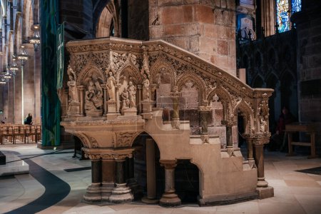 Un púlpito de piedra intrincadamente tallado dentro de la catedral de St Giles en Edimburgo, que muestra detalles arquitectónicos góticos y esculturas religiosas.
