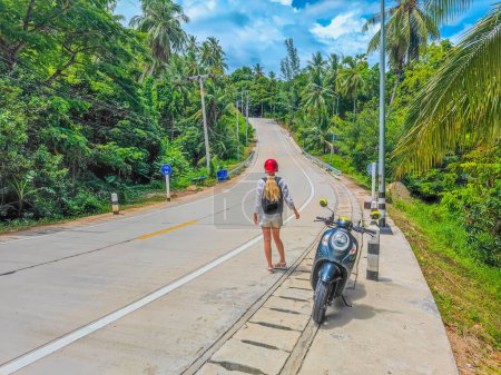 Photo for Beautiful young traveler woman with helmet and scooter in countryside in Koh Phangan, Thailand having a break on the road and enjoying nature - Royalty Free Image