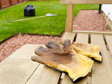 Photo for Garden gloves on garden seat and raked leaves in black bag UK - Royalty Free Image