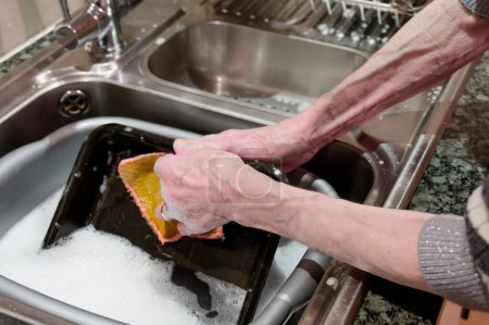 Photo for Elderly female washing kitchen oven tray at sink UK - Royalty Free Image