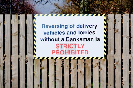 Reversing of delivery vehicles safety sign on fence at construction site UK