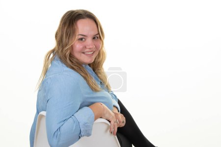 Téléchargez les photos : Jeune en surpoids belle femme potelée blonde aux cheveux longs s'asseoir sur une chaise sur fond blanc - en image libre de droit