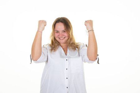 Téléchargez les photos : Young beautiful woman blonde oversize wearing casual shirt white on white background very happy and excited doing winner gesture with arms raised smiling and screaming for success celebration - en image libre de droit