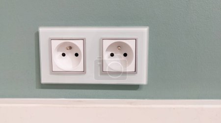 Foto de Two white french european electrical outlets with plug inserted into modern neutral green wall with copy space banner - Imagen libre de derechos