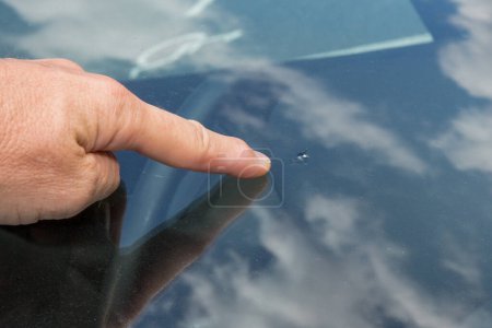 Photo for Glazier windscreen man finger indicates the impact on the broken car windshield - Royalty Free Image