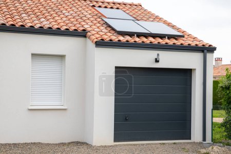 Téléchargez les photos : Façade de maison moderne avec volet fermé de porte de garage avec panneau solaire sur le toit à l'entrée de la maison privée - en image libre de droit