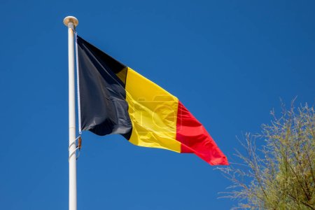 Belgische Flagge Belgische Flagge auf dem Mast im Wind und blauem Himmel