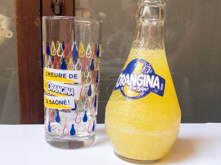 Foto de Burdeos, Francia - 09 18 2023: Orangina logo texto y signo de marca en botella de limonada naranja y vidrio en mesa de bar - Imagen libre de derechos